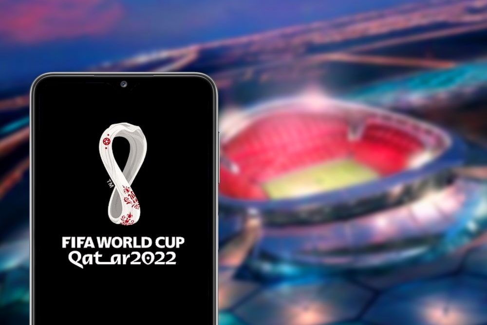 Firfa Wrold Cup logo on a mobile screen, with blurry stadium in the background